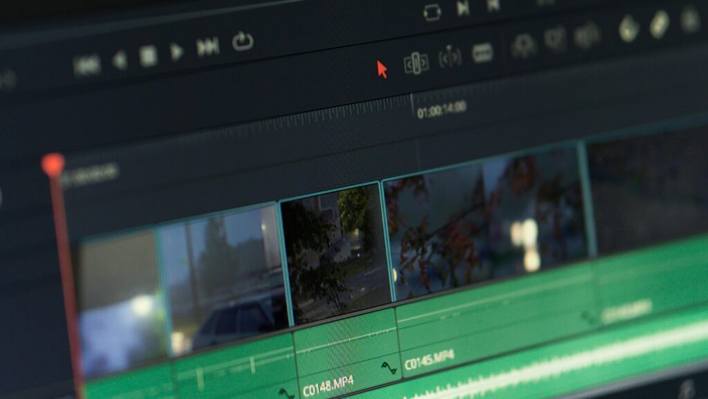 Close-up view of a video editing software interface on a computer monitor, displaying a timeline with multiple clips and a green audio waveform at the bottom. The playhead is positioned at one minute and four seconds on the timeline, and the screen is slightly out of focus, emphasizing the video editing process.